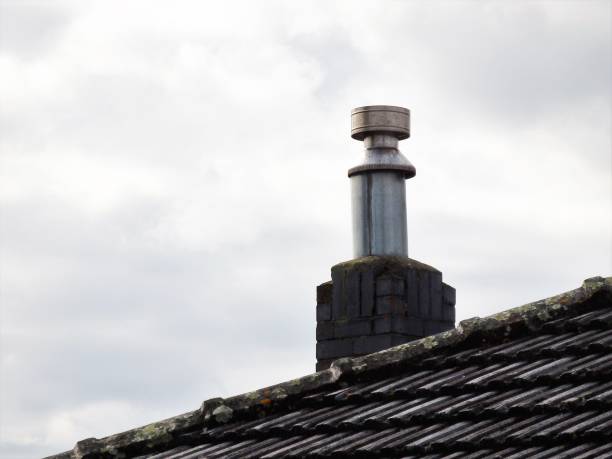 Brown brick chimney on a brown tiled against a cloudy blue sky